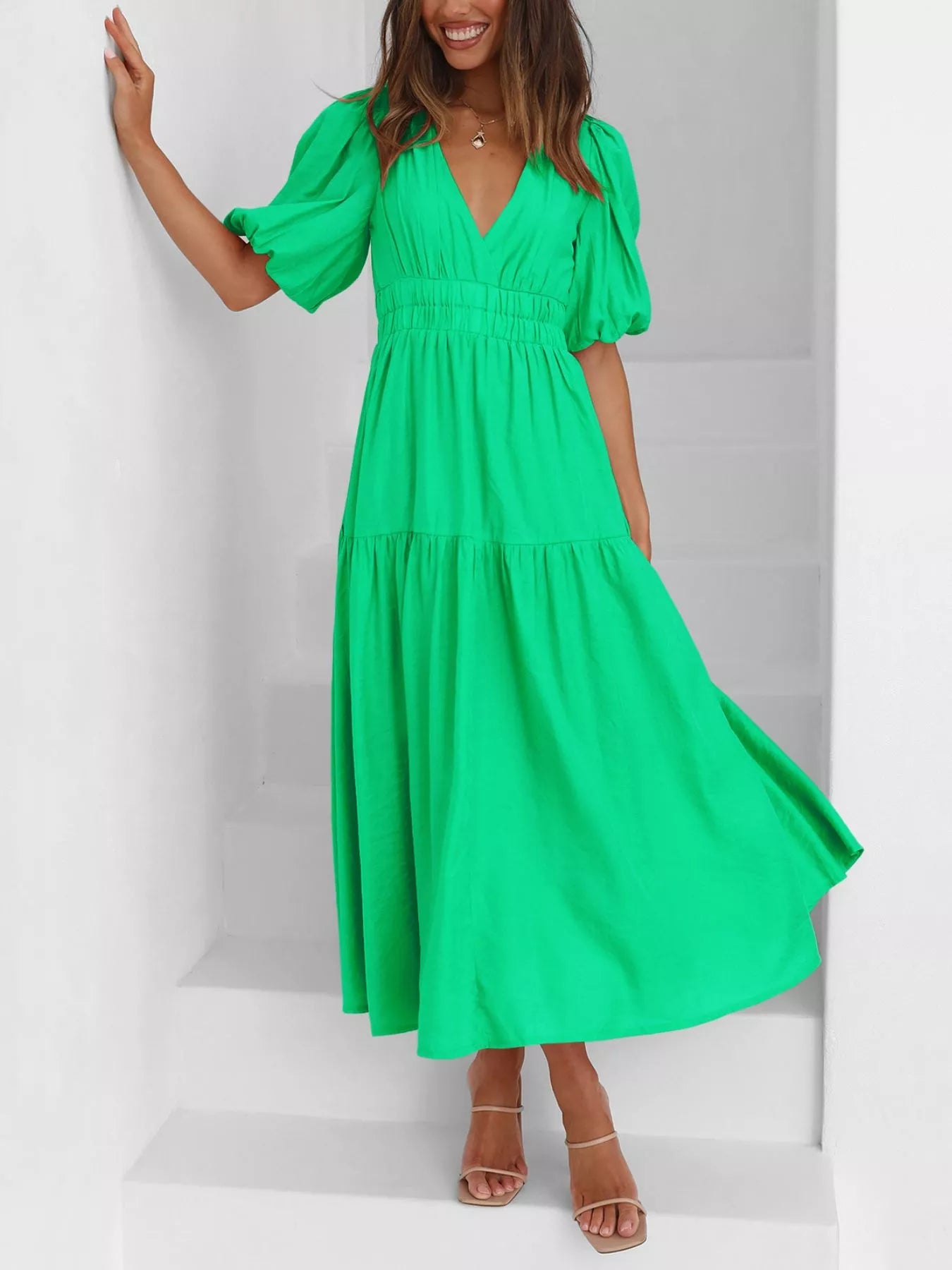 A woman wearing a bright green midi dress with puff sleeves, a V-neckline, and a tiered skirt, standing on white stairs.