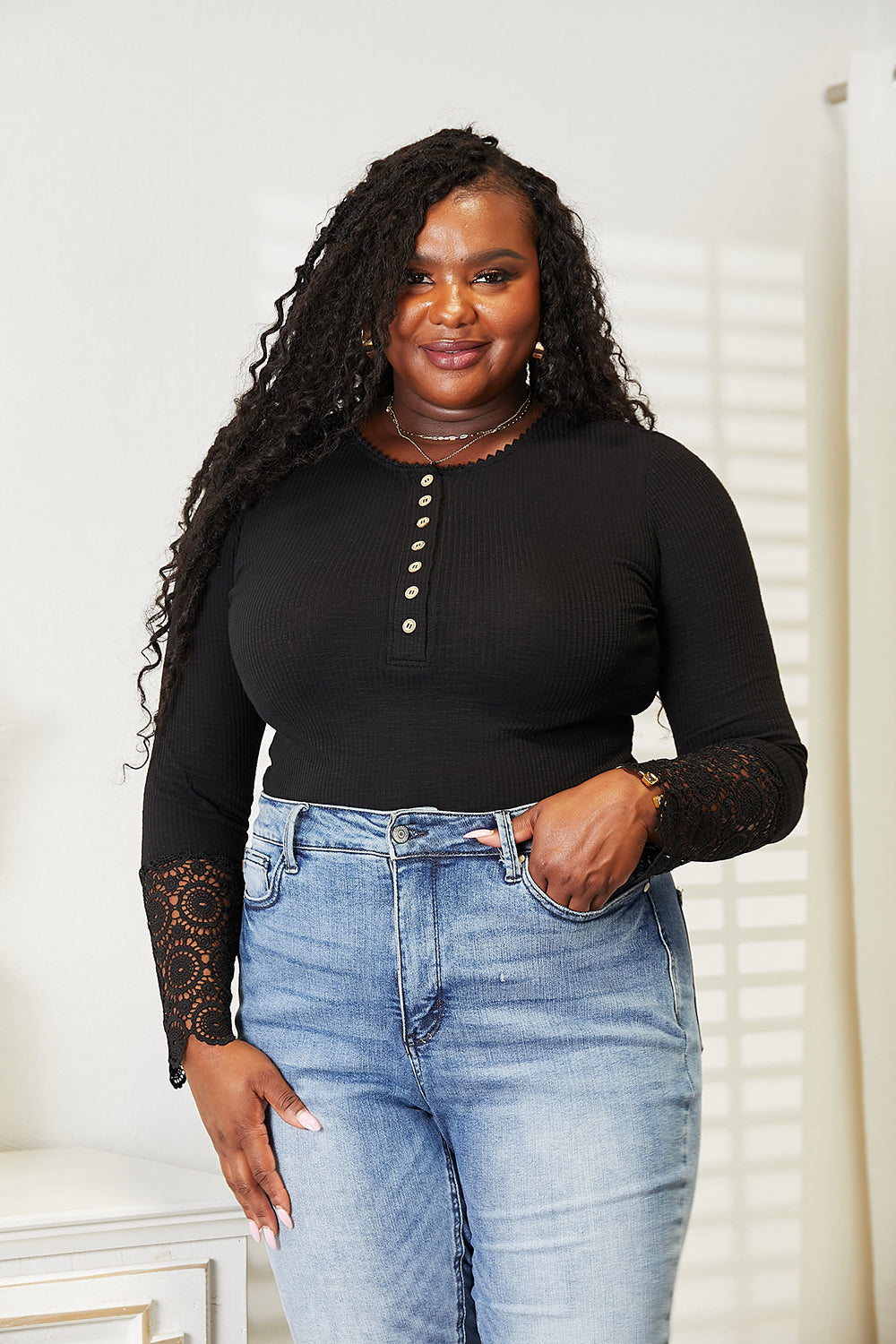 Woman wearing a black long-sleeve top with lace sleeves and light blue jeans indoors.