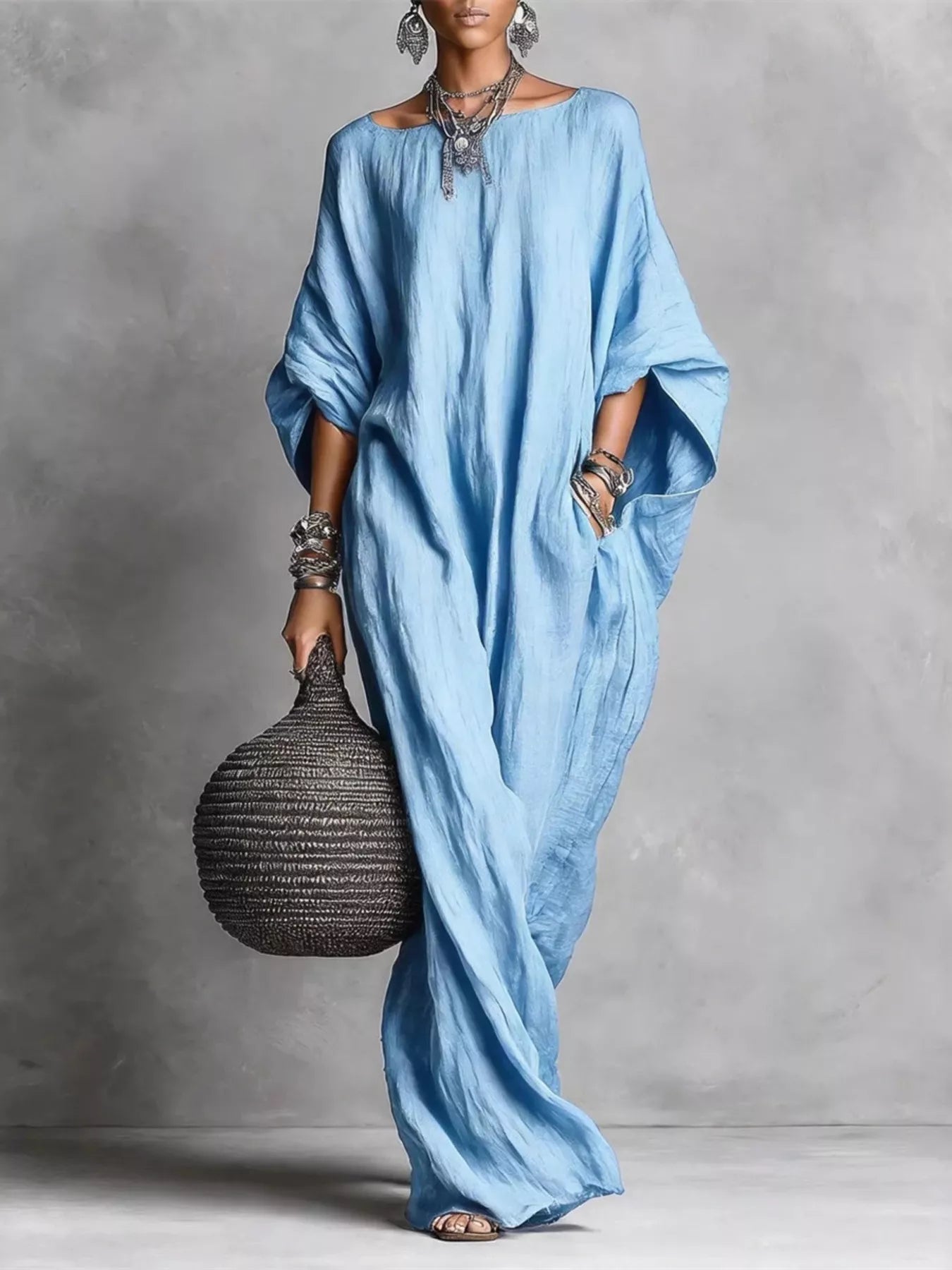 Woman wearing a blue dress holding a black woven bag against a gray background
