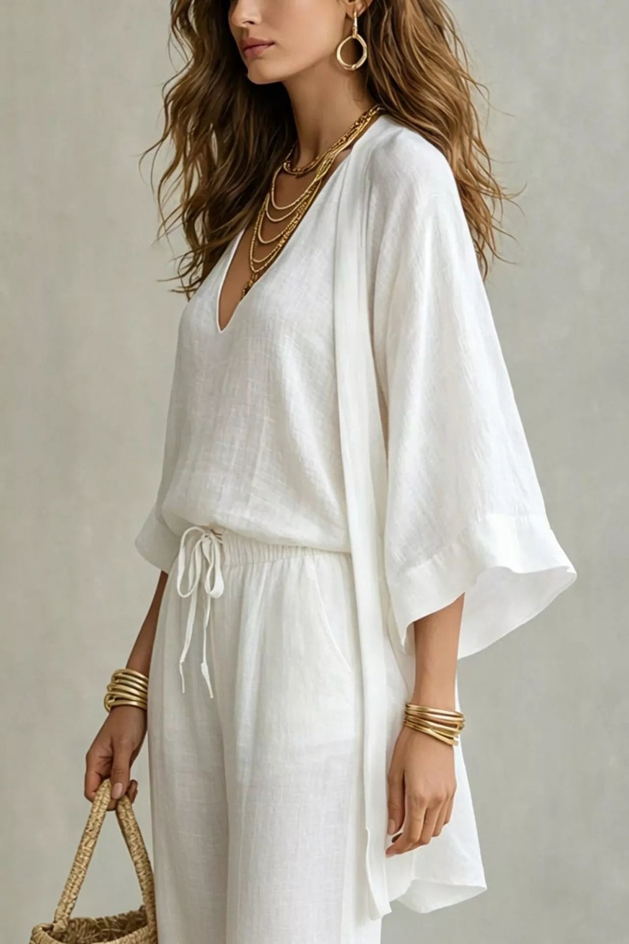 Woman wearing a white three-piece set with open-front kimono cardigan, V-neck cami, and wide-leg drawstring pants, holding a woven tote bag