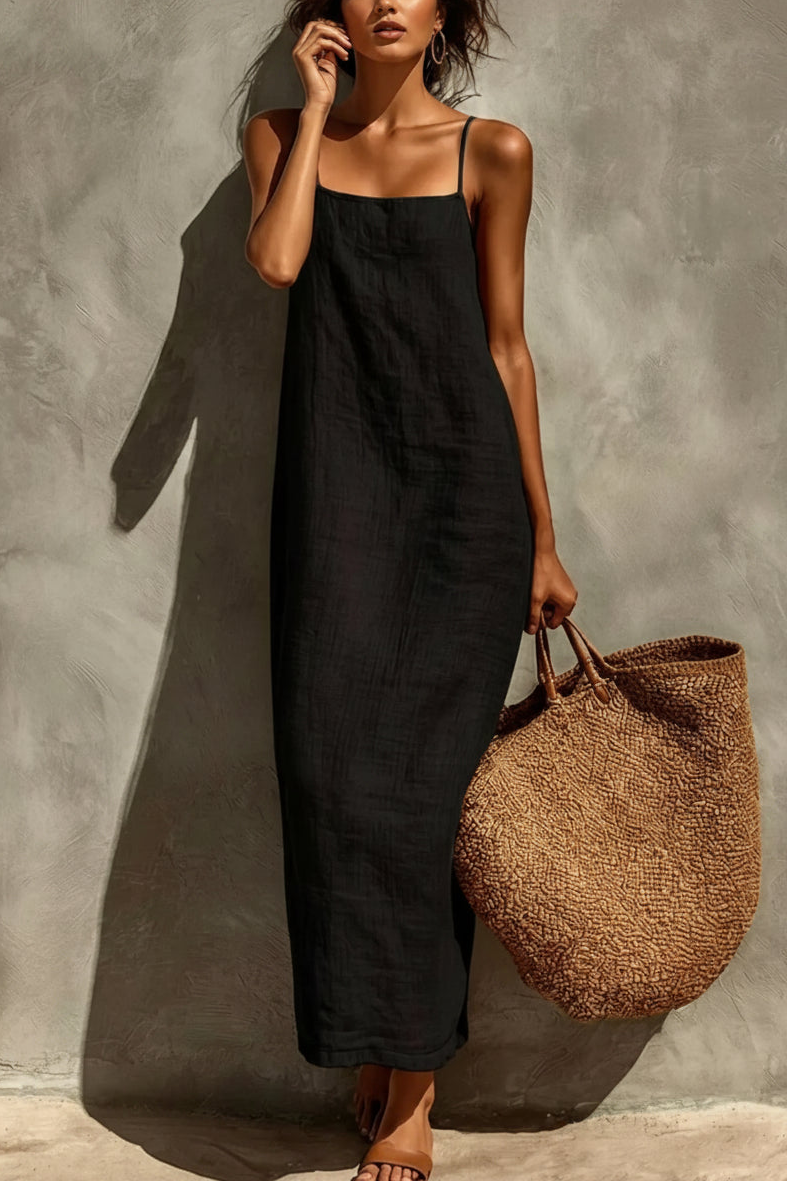 Woman in a black dress holding a woven bag against a textured wall.