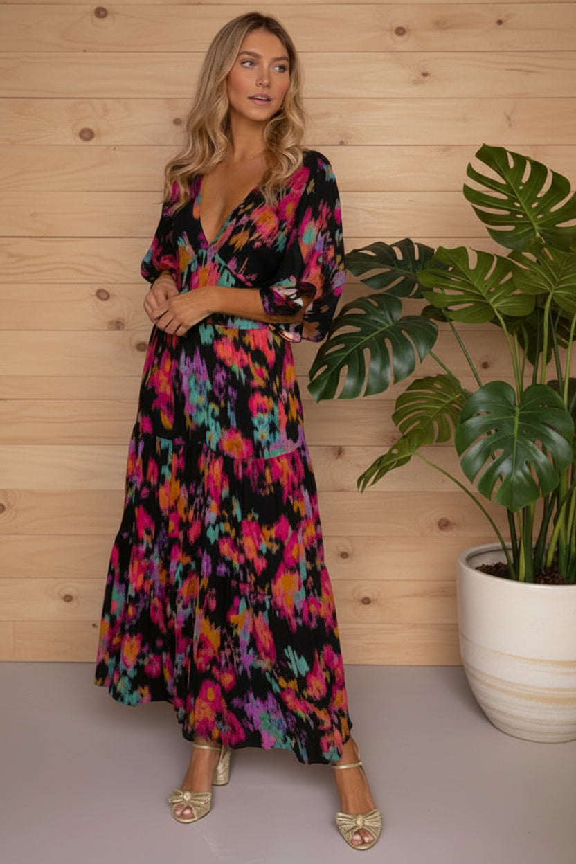Woman wearing a colorful dress standing next to a potted plant against a wooden wall.