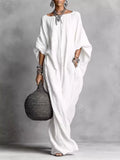 Woman in a long white dress holding a textured black handbag against a gray background
