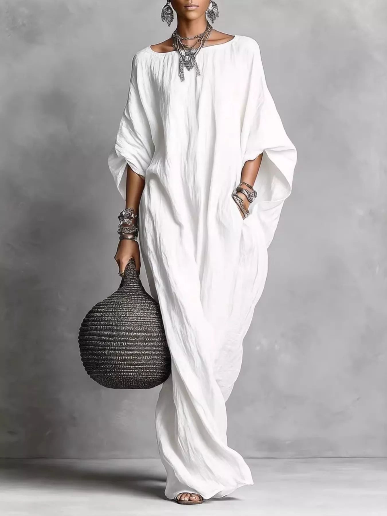 Woman in a long white dress holding a textured black handbag against a gray background