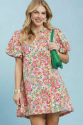 Woman wearing a colorful patterned dress holding a green bag against a light blue background