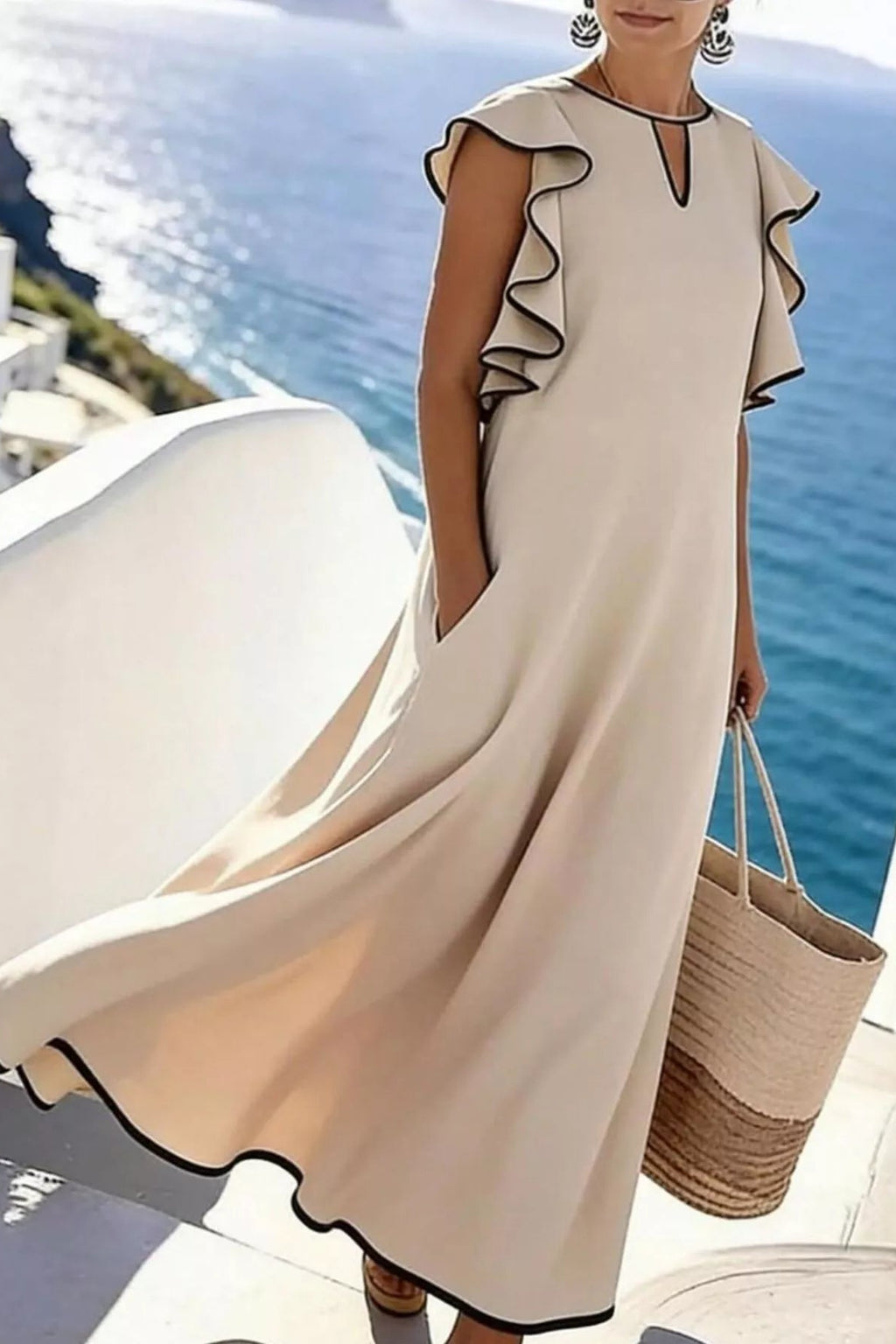 Woman wearing a beige dress with ruffled sleeves by the ocean.