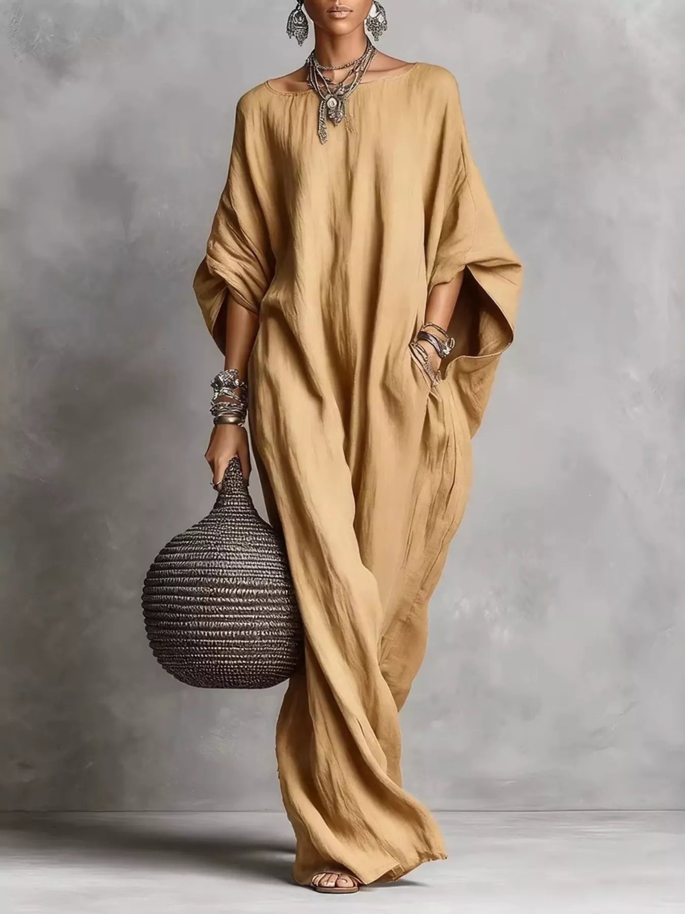 Woman in a long beige dress holding a textured bag against a gray background
