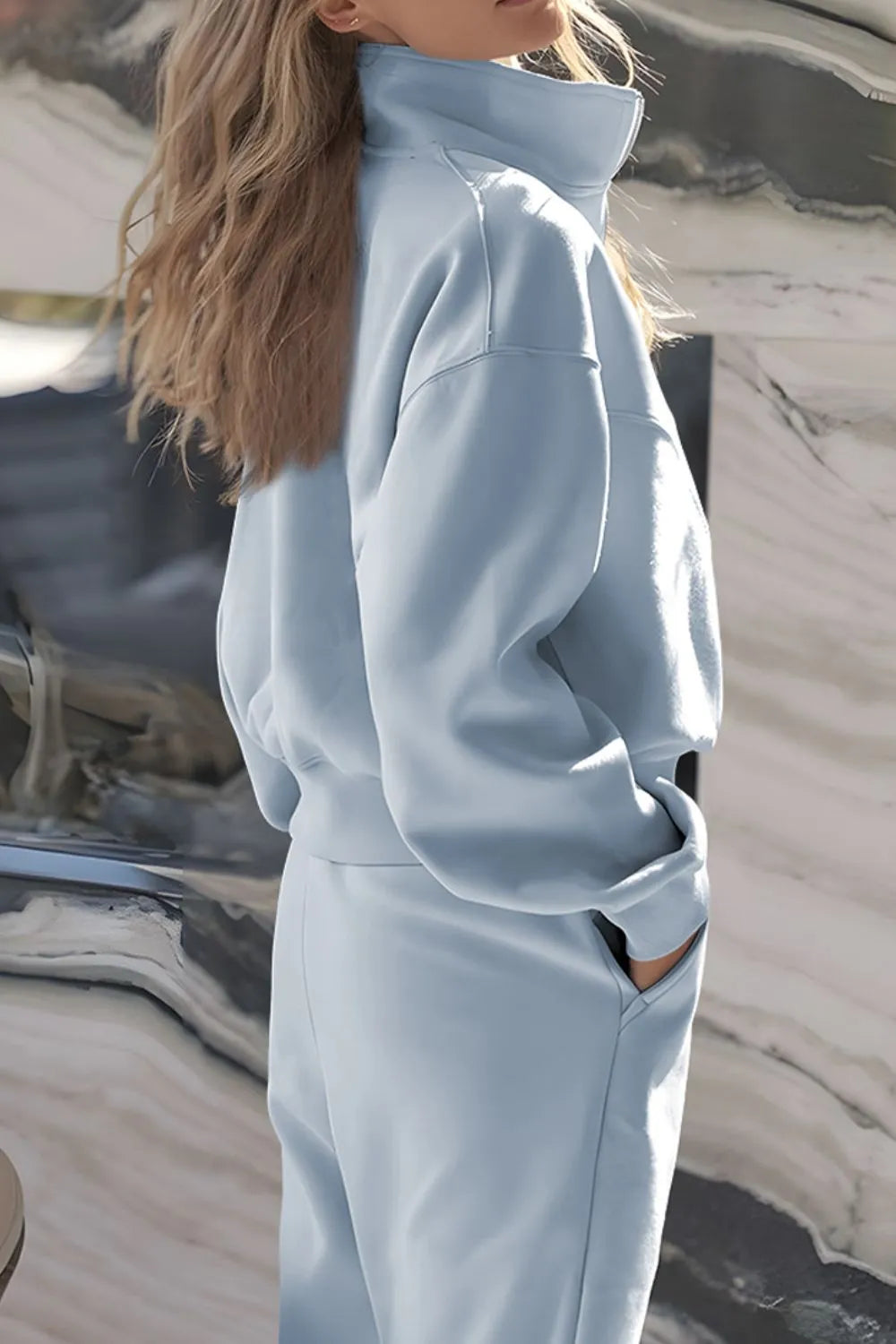 Person wearing a light blue tracksuit standing in front of a reflective surface.