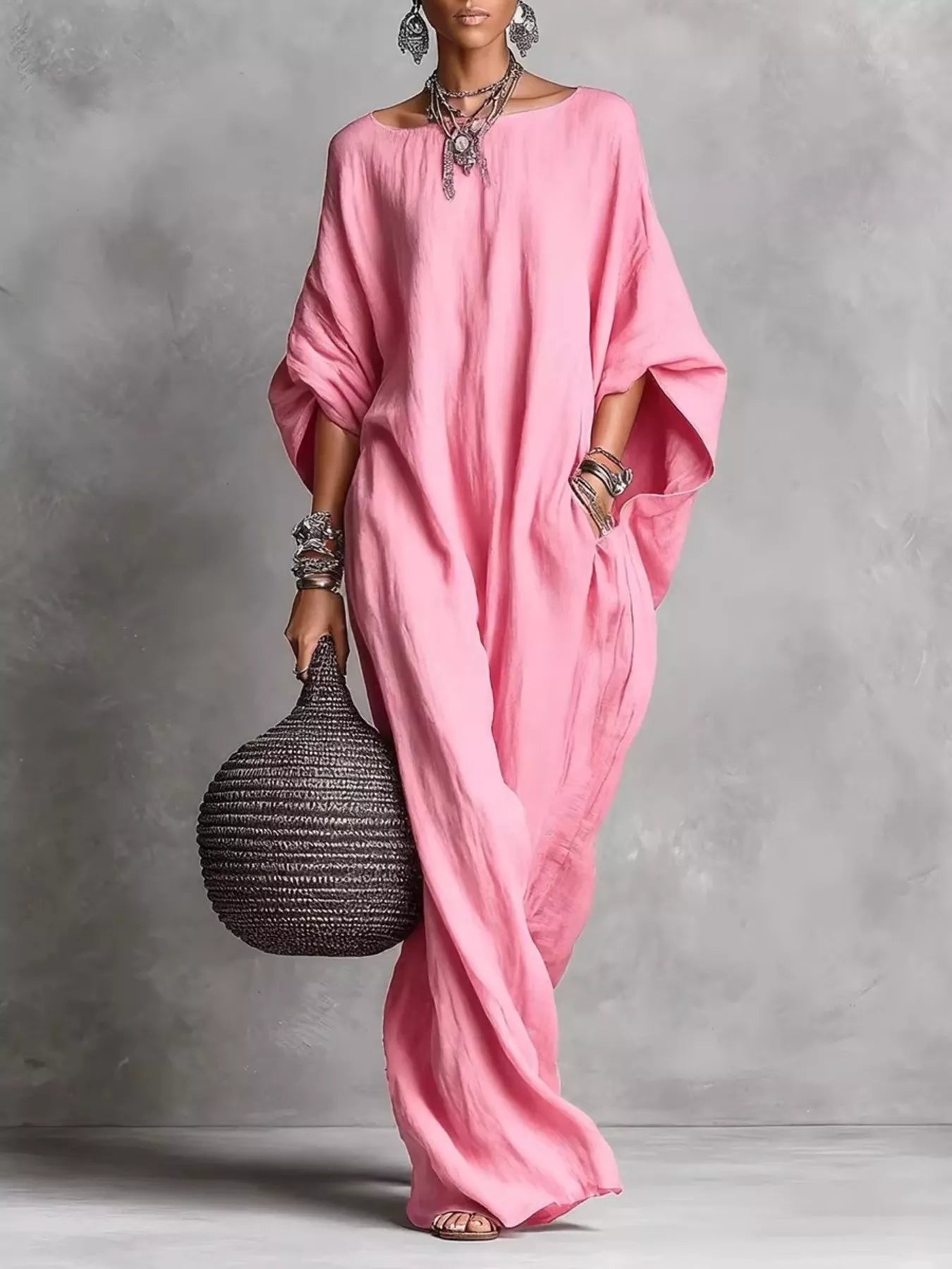 Woman in a pink dress holding a woven bag against a gray background