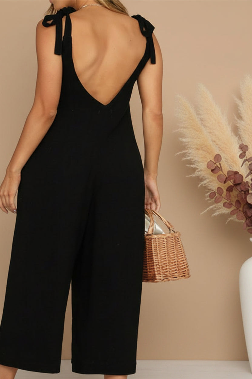 Person wearing a black jumpsuit with wide-leg pants and a minimal background