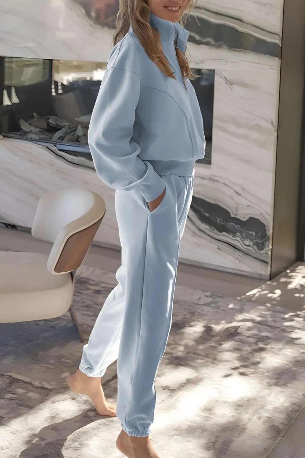 Person wearing a light blue tracksuit standing in front of a marble wall.