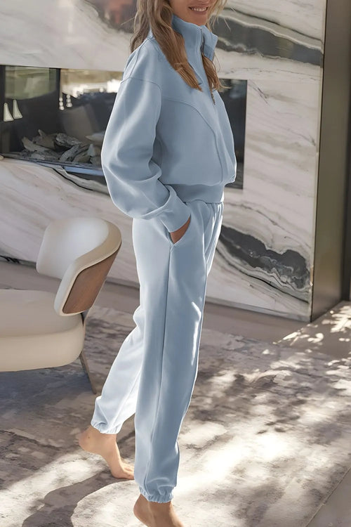 Person wearing a light blue tracksuit standing in front of a marble wall.