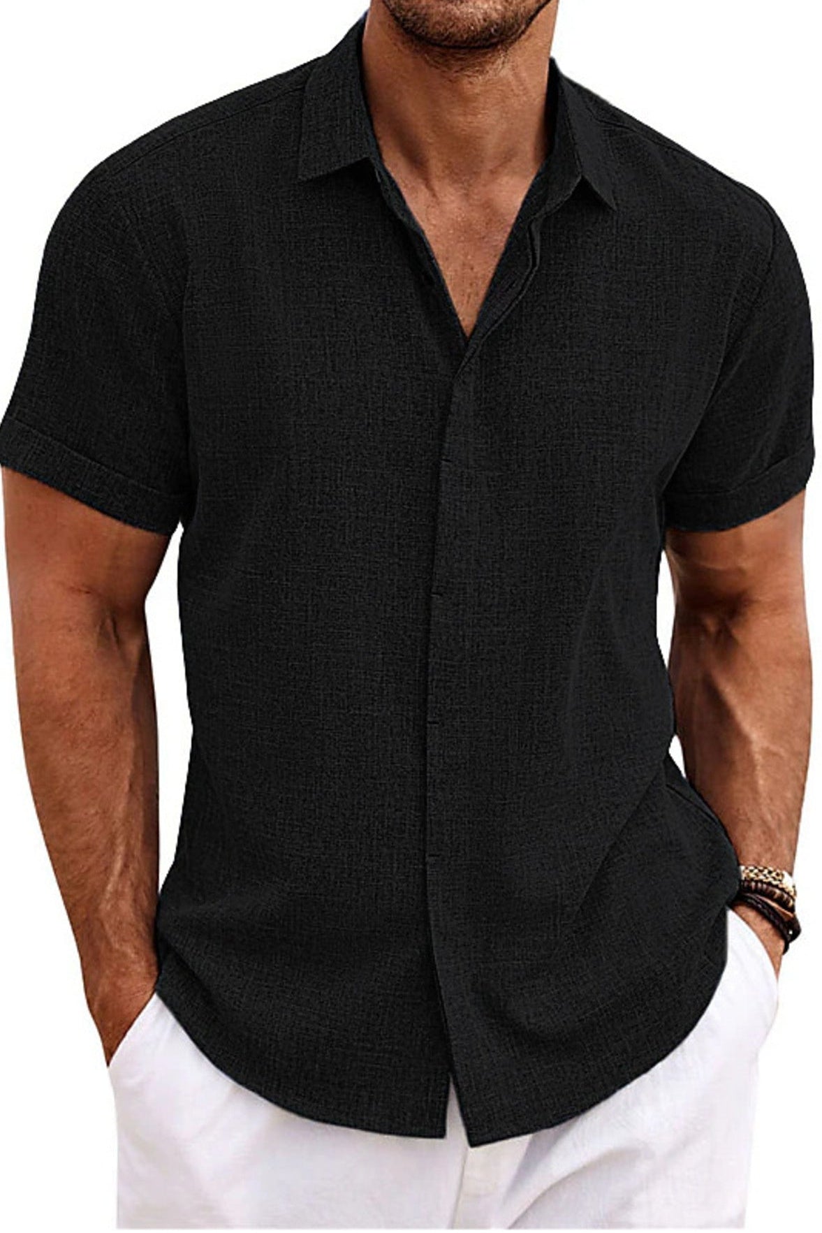 Man wearing a black short-sleeve button-up shirt with white pants on a white background