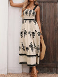 A woman models a sleeveless, one-shoulder maxi dress with a cream base and black floral patterns, standing against a white wall and dark wooden door.