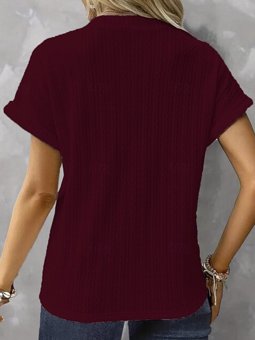 A woman wearing a short-sleeve ribbed knit top in deep burgundy, shown from the back against a gray textured background.