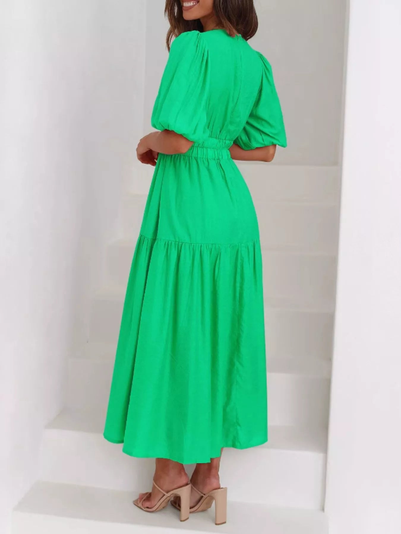 A woman wearing a bright green tiered maxi dress with puff sleeves and a gathered waist, standing on white stairs.