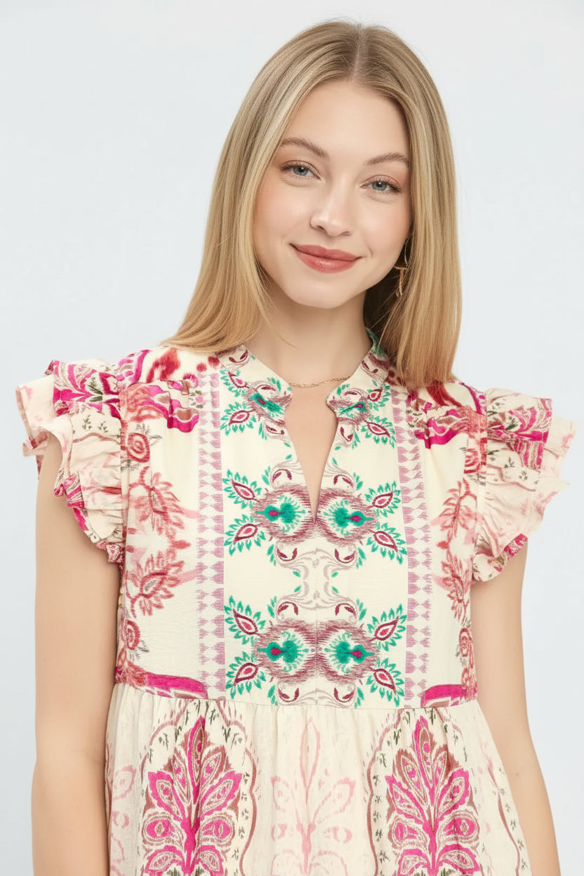 A woman wearing a cream-colored bohemian-style dress with vibrant pink, teal, and green floral patterns, shown in a close-up shot.