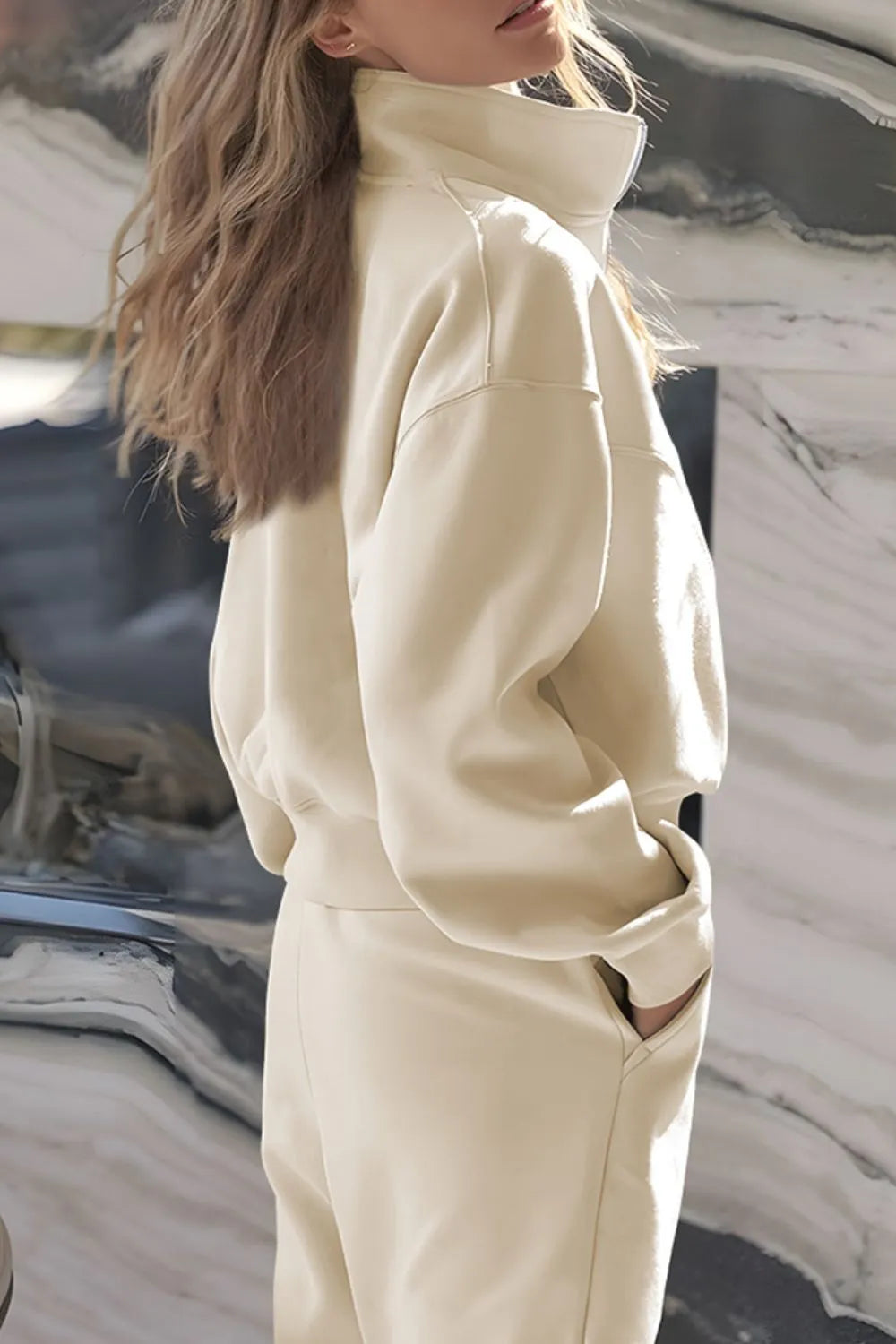 Person wearing a beige tracksuit against a marble background