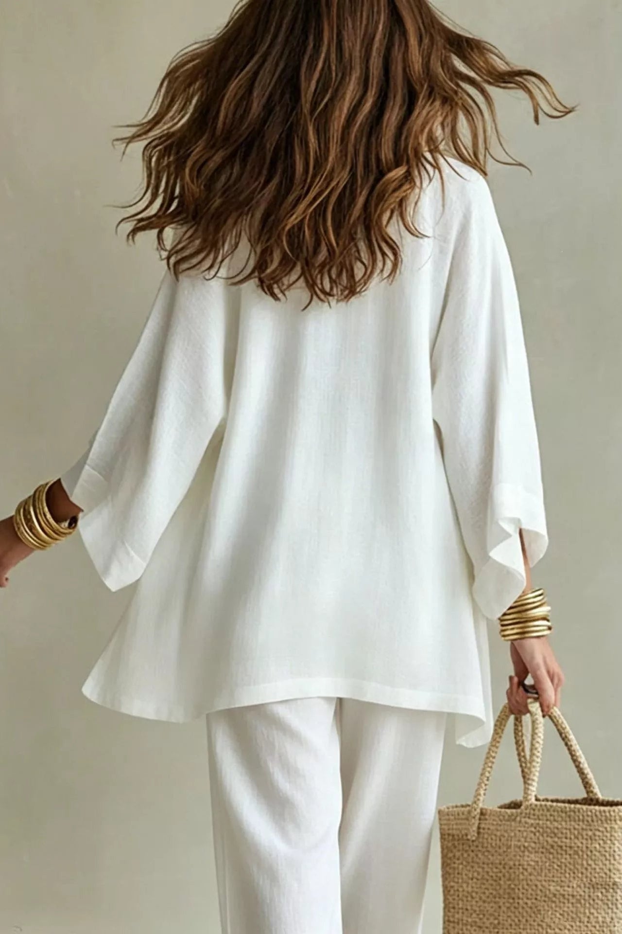 Woman wearing a white three-piece set with open-front kimono cardigan, V-neck cami, and wide-leg drawstring pants, holding a woven tote bag