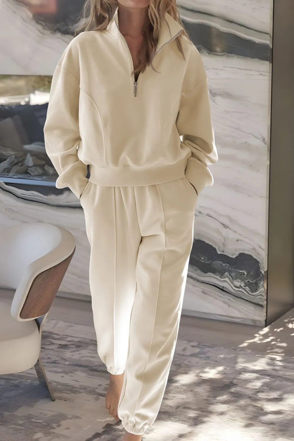 Person wearing a beige tracksuit in a room with marble walls.