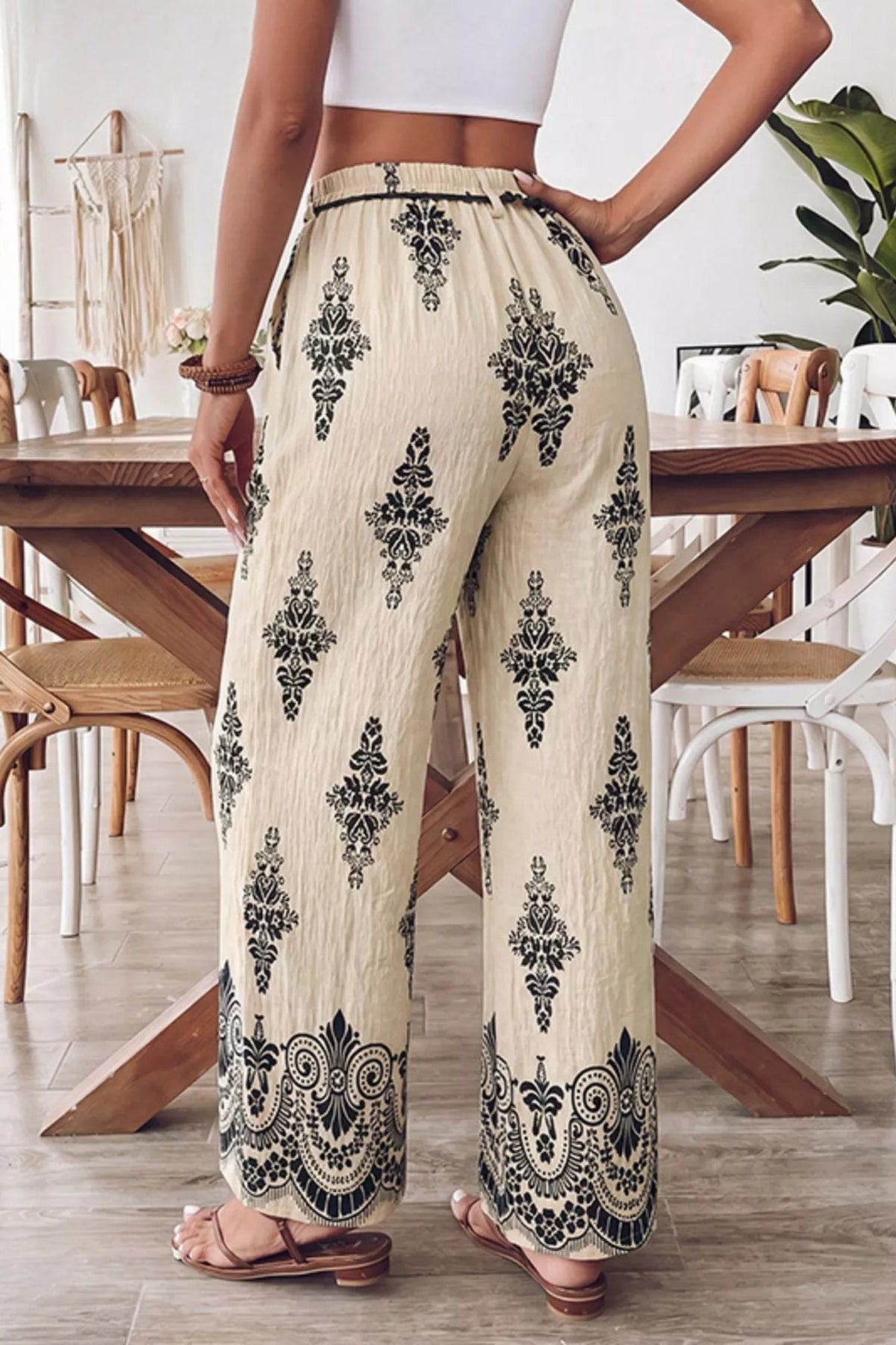 Person wearing cream-colored pants with black floral patterns in a dining room setting.