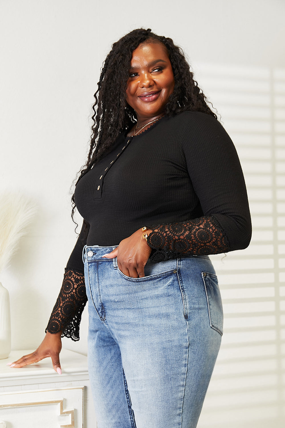 Female wearing a black top with lace sleeves and blue jeans white background