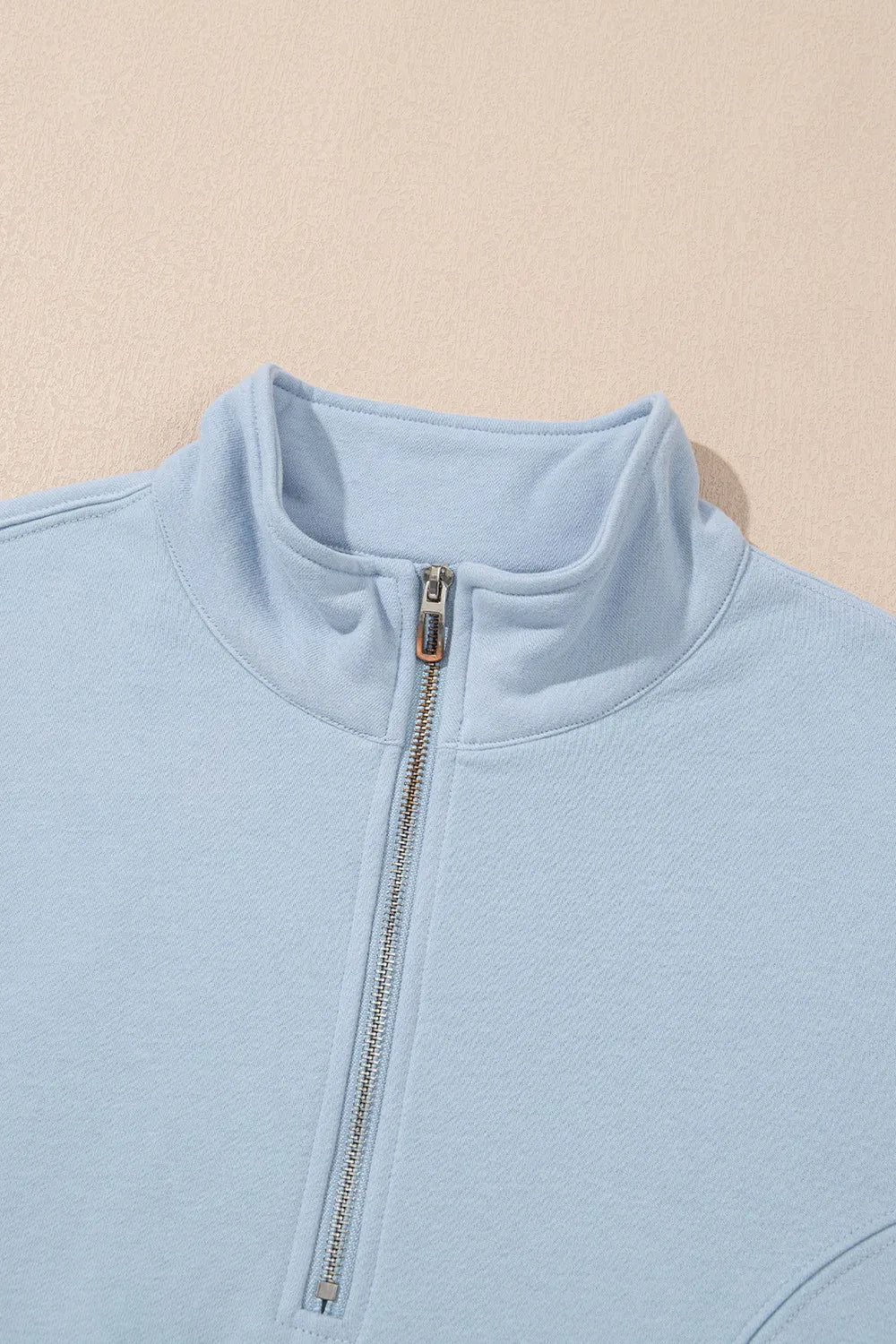 Light blue fleece jacket with a zipper on a beige background